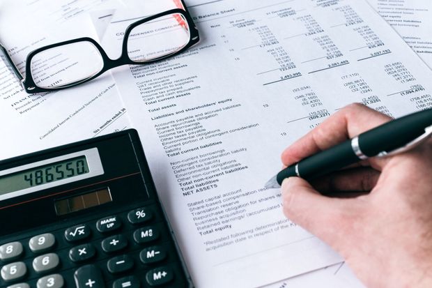 Escritura a mano en documento financiero, calculadora que muestra $486,550, anteojos al costado.