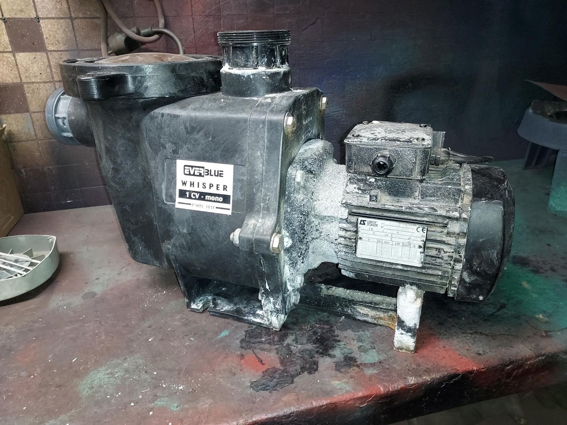 Pompe de piscine noire avec moteur, sur un établi, avec résidus blancs.