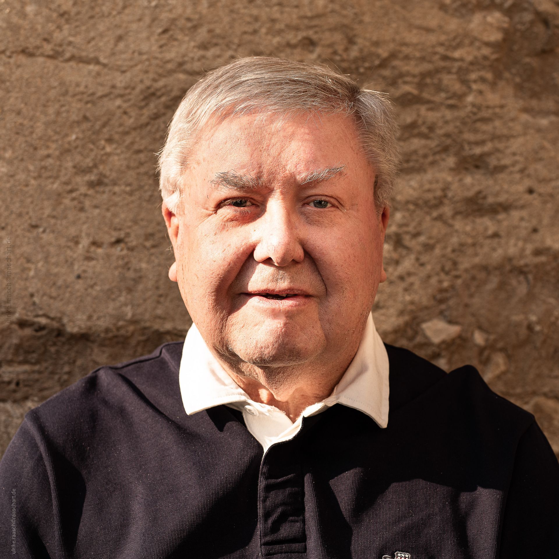 Ein Mann in einem schwarzen Pullover und einem weißen Hemd lächelt in die Kamera.