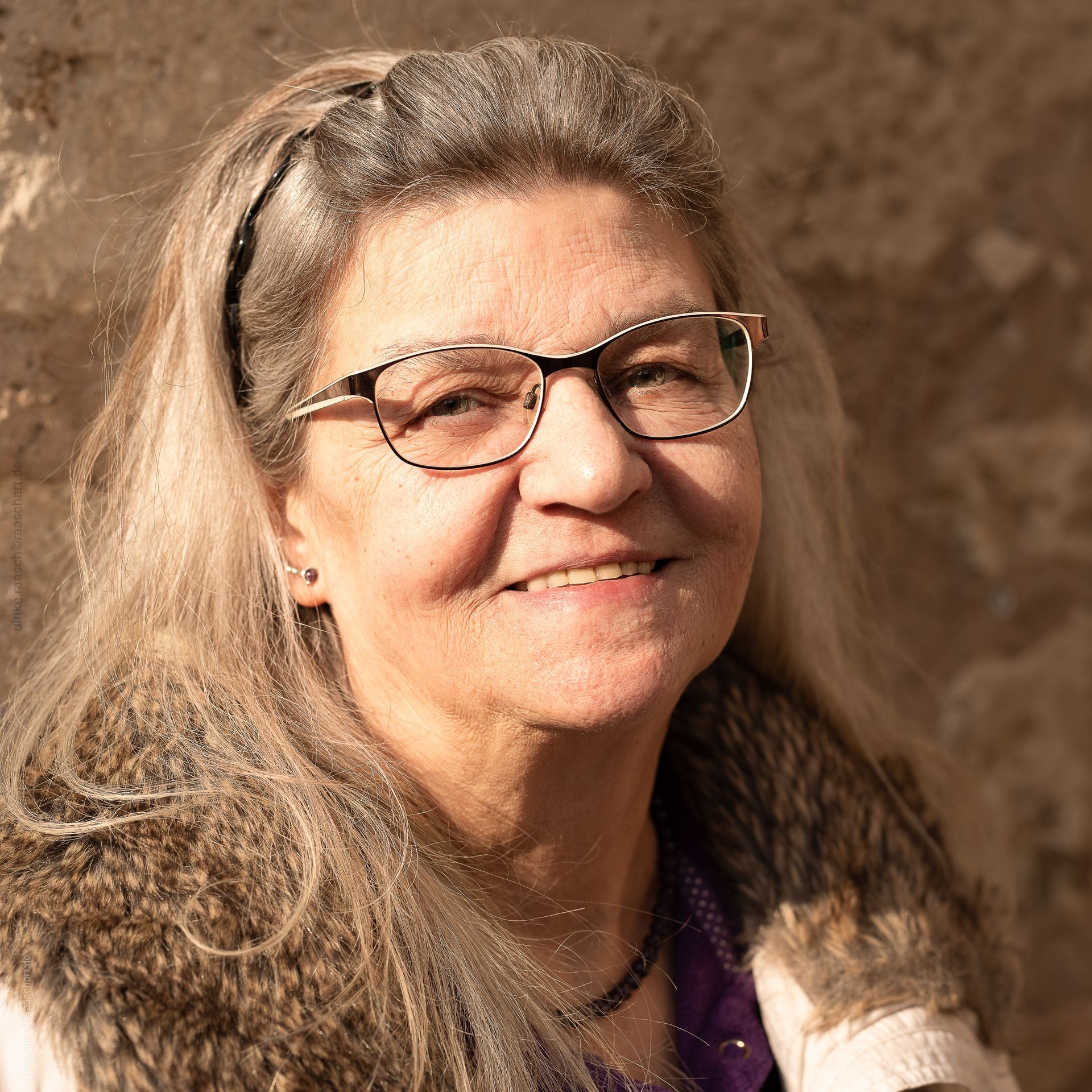 Eine Frau mit Brille und Pelzmantel lächelt in die Kamera.