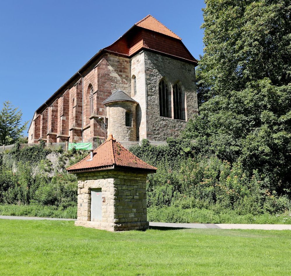Ein Backsteingebäude mit einem roten Ziegeldach ist von Bäumen und Gras umgeben.