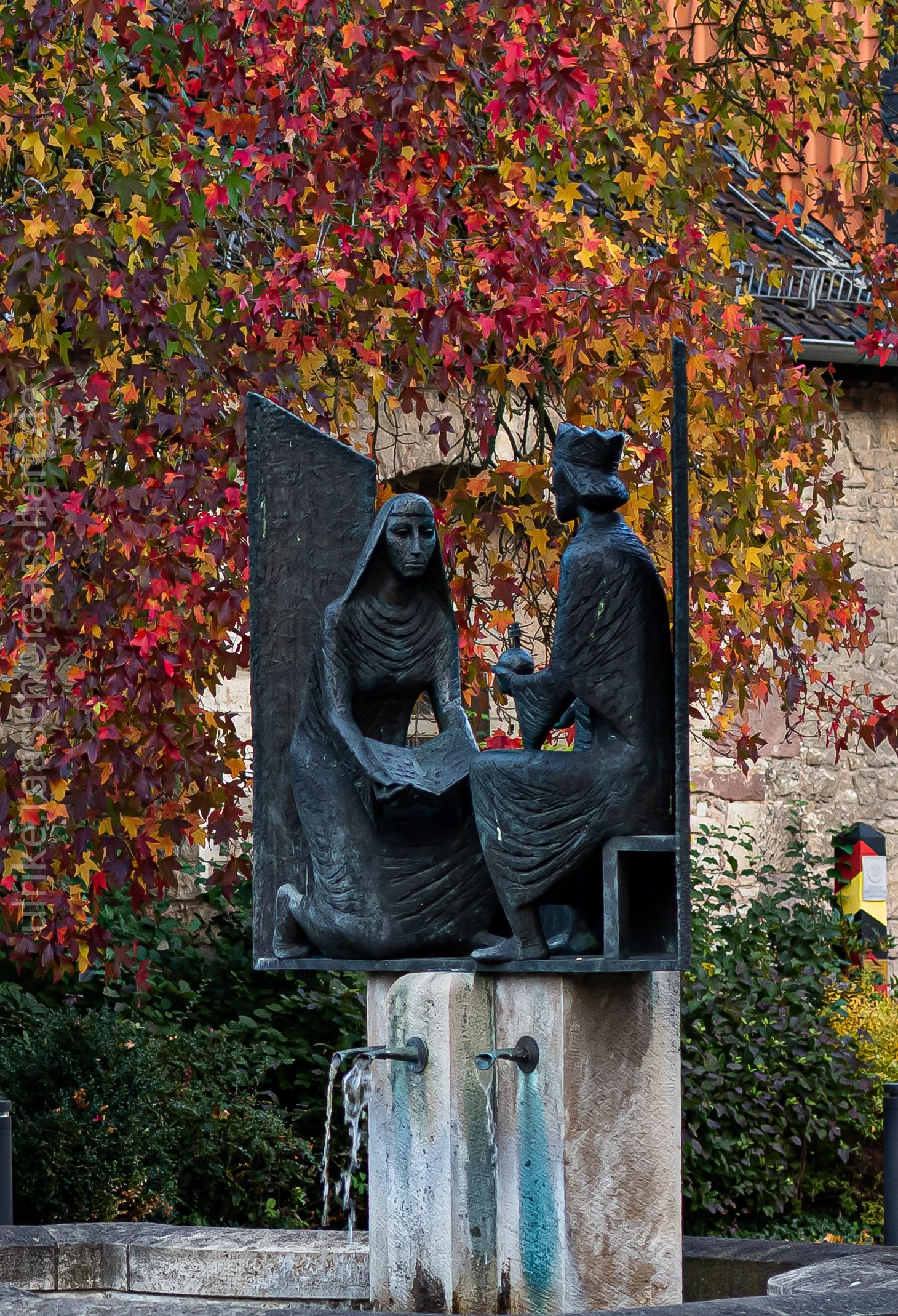 Eine Statue eines Mannes und einer Frau, die nebeneinander vor einem Brunnen sitzen.