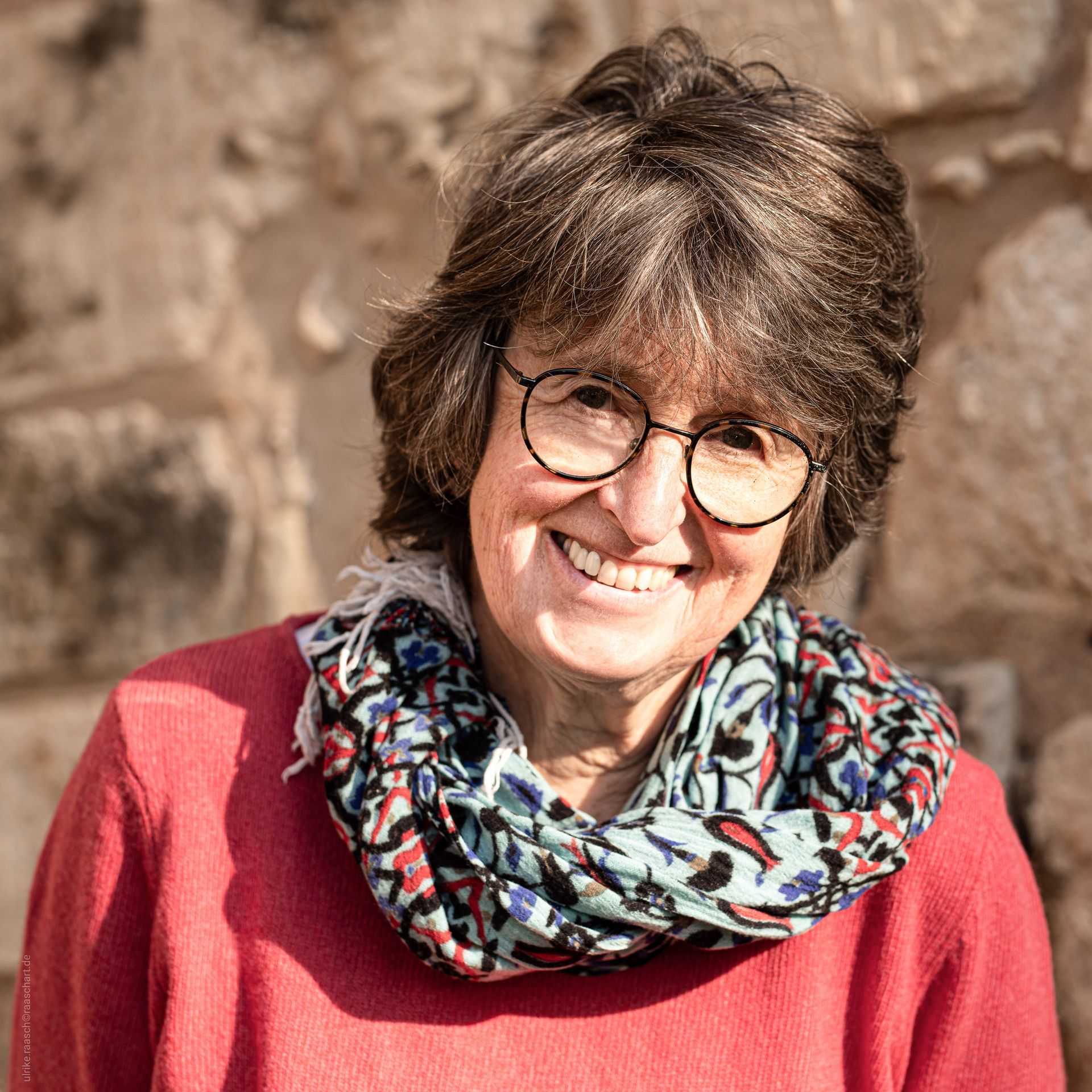 Eine Frau mit Brille und Schal lächelt in die Kamera.