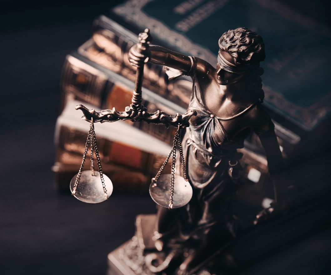 Statue de la justice avec balance, bandeau et livres en arrière-plan. Tons bronze.