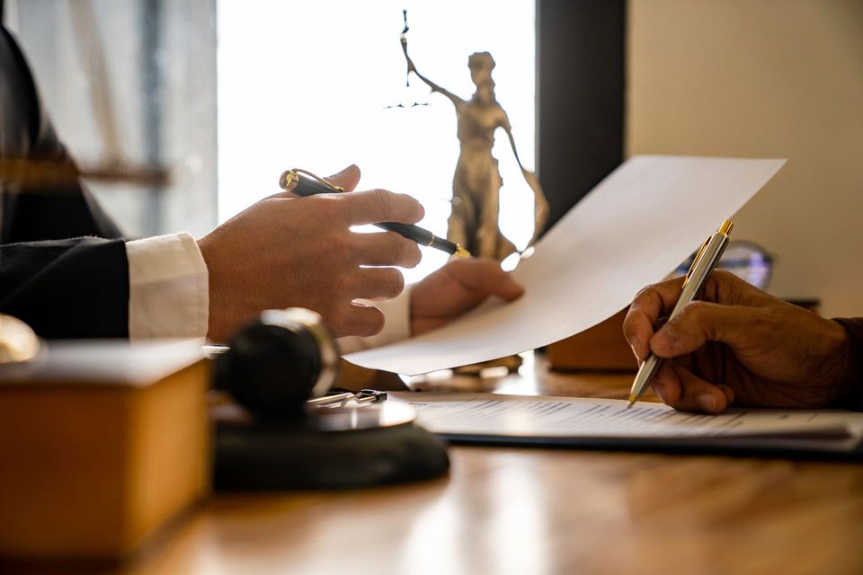 Un avocat examine un document avec son client et signe un contrat. Une statue de la justice apparaît en arrière-plan.