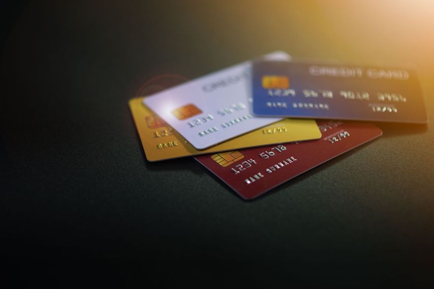 Quatre cartes de crédit empilées sur une surface sombre ; cartes blanches, dorées, bleues et rouges visibles.