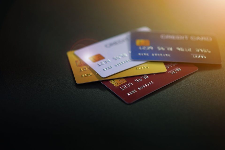 Quatre cartes de crédit empilées sur une surface sombre ; cartes blanches, dorées, bleues et rouges visibles.