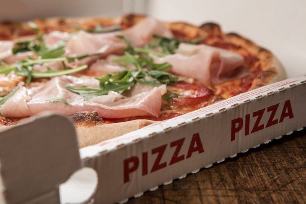 Pizza à emporter garnie de pepperoni, de prosciutto et de roquette dans une boîte blanche.