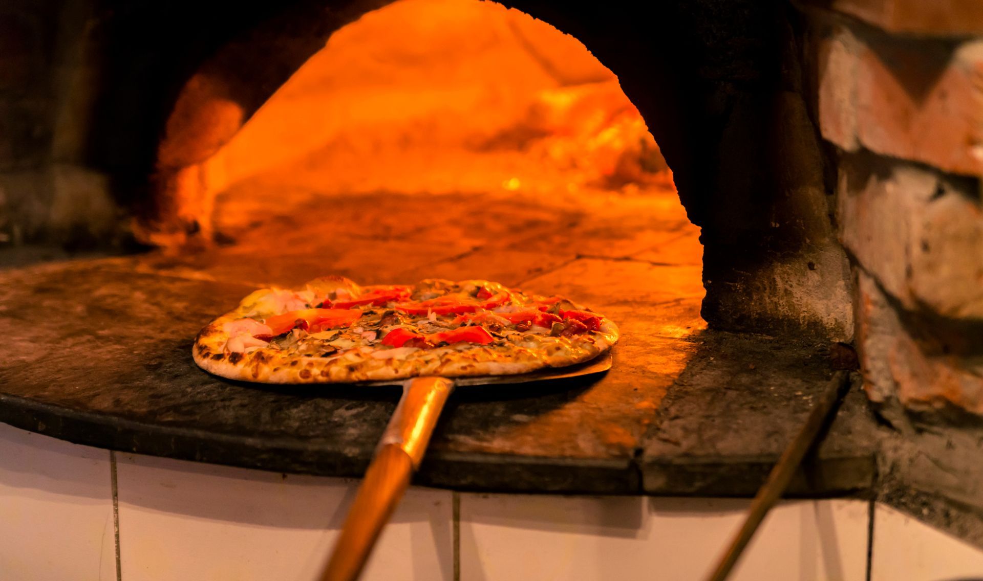 Pizza en train de cuire dans un four à bois sur une pelle à pizza.