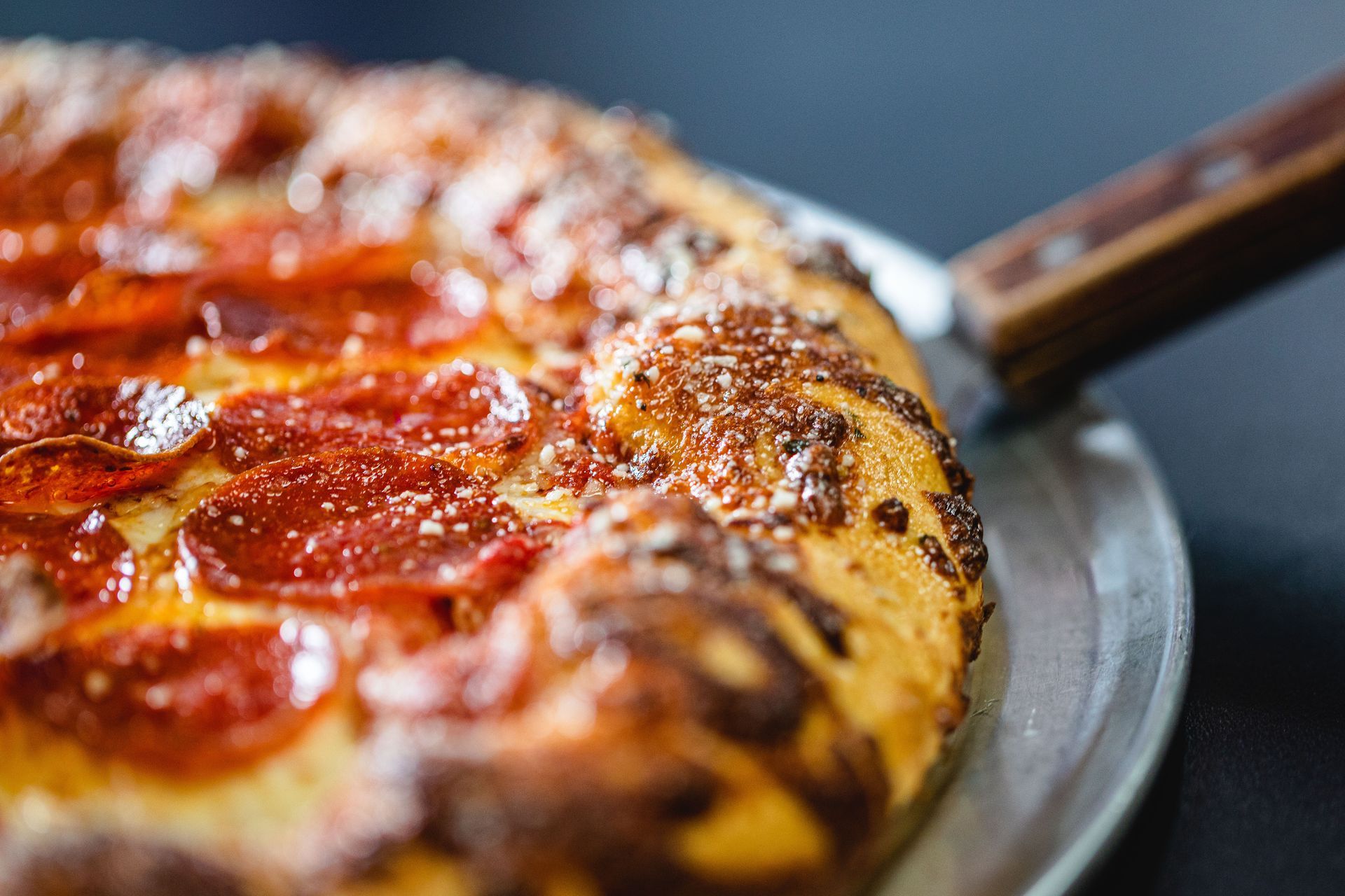 Pizza pepperoni sur une plaque en métal avec un manche en bois.