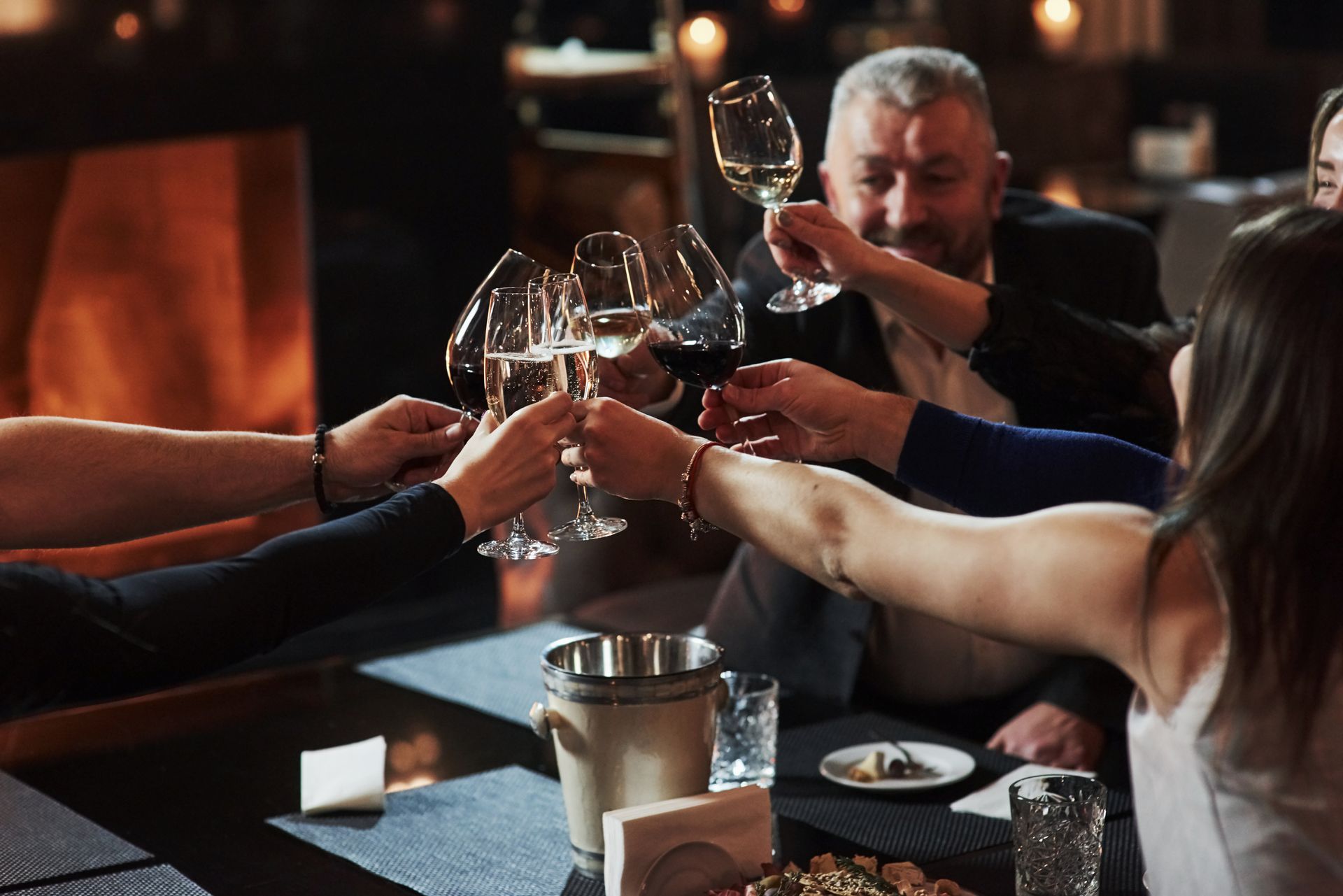 Des amis trinquent avec des verres de vin autour d'une table de restaurant près d'une cheminée.
