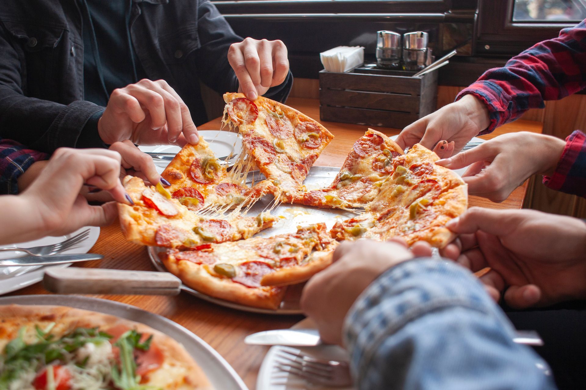 Des personnes partageant des parts de pizza au fromage autour d'une table.