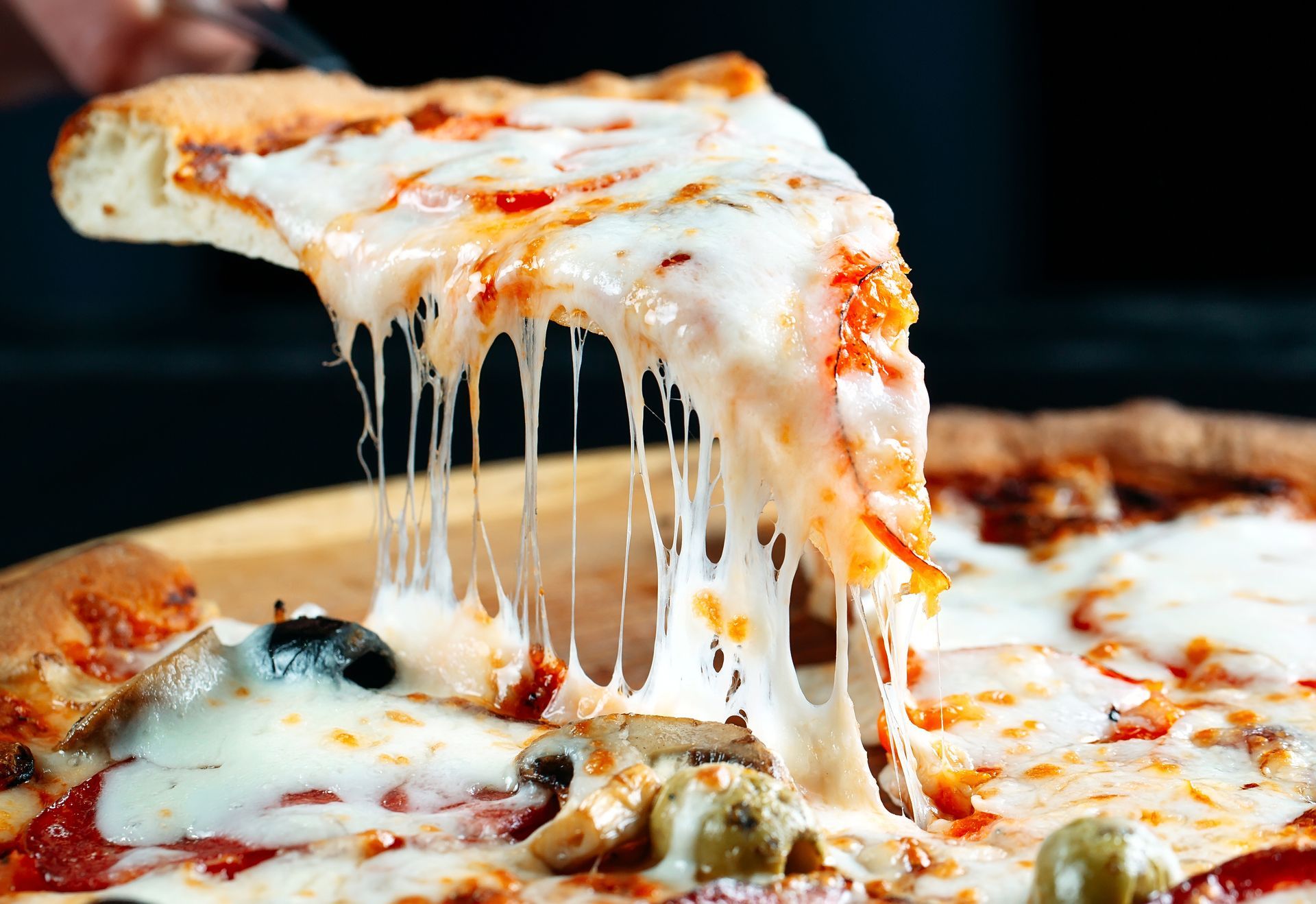 Une part de pizza au fromage est soulevée, le fromage fondu s'étirant depuis la pizza.