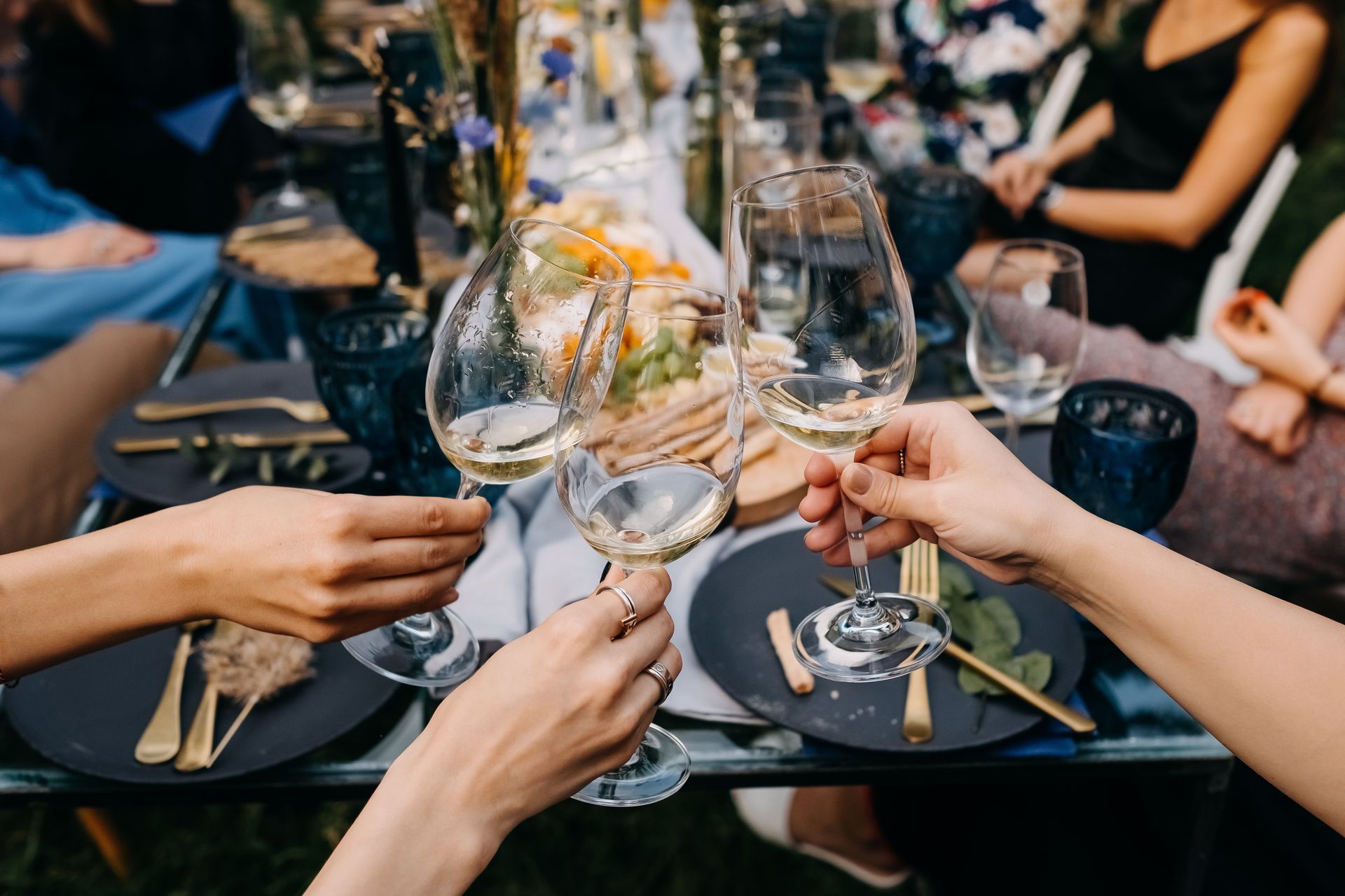 Des mains lèvent leurs verres à vin au-dessus d'une table dressée avec des assiettes et des bougies lors d'un repas.