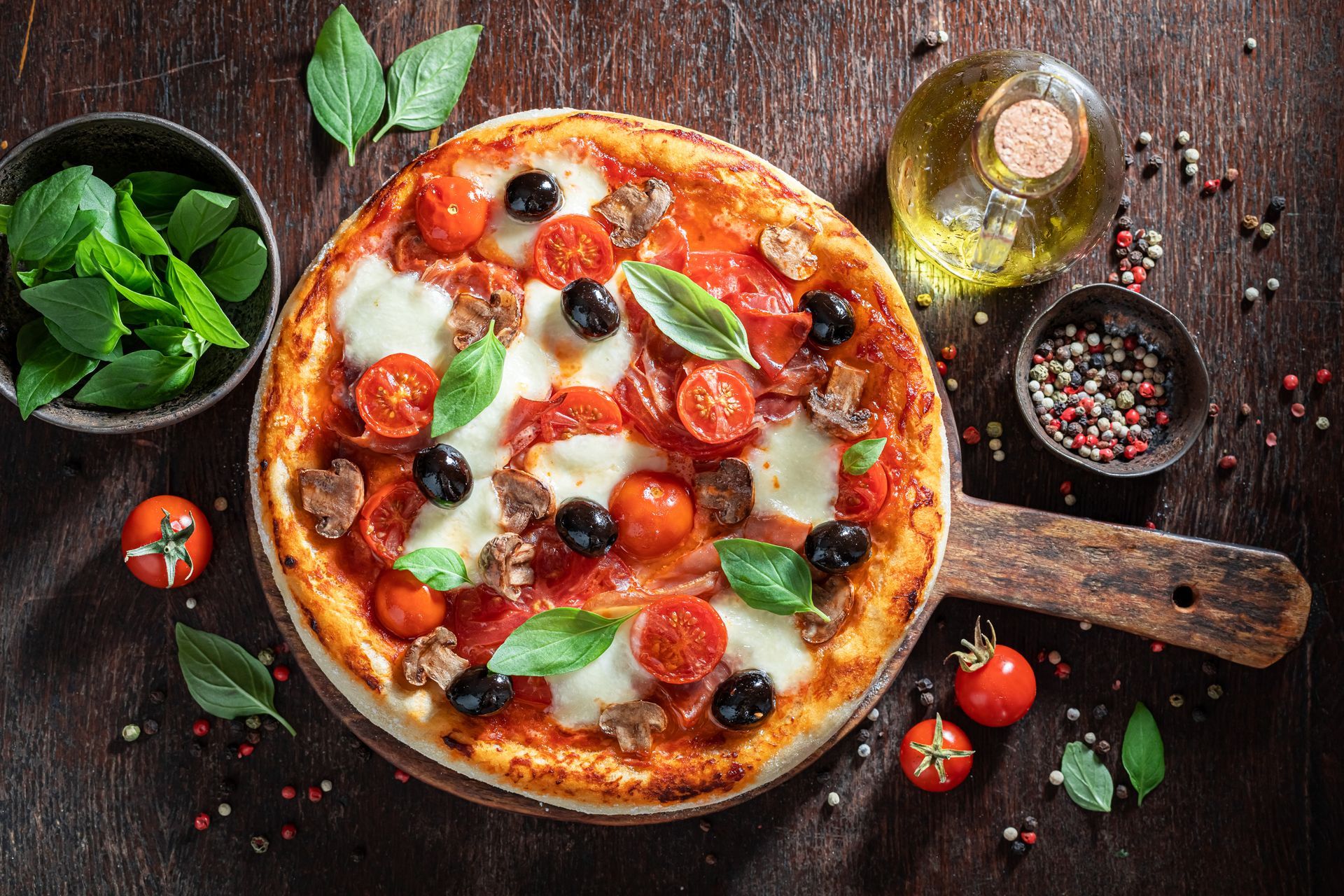 Pizza rustique aux tomates, basilic, olives et un verre d'huile d'olive sur une table en bois.