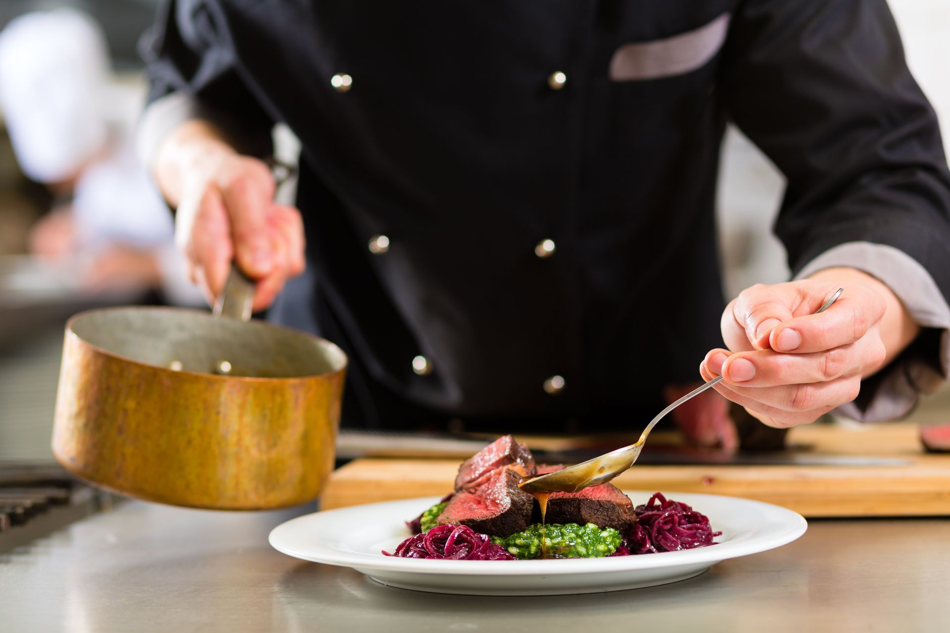 Un chef dresse un plat gastronomique coloré avec sa sauce dans une cuisine.