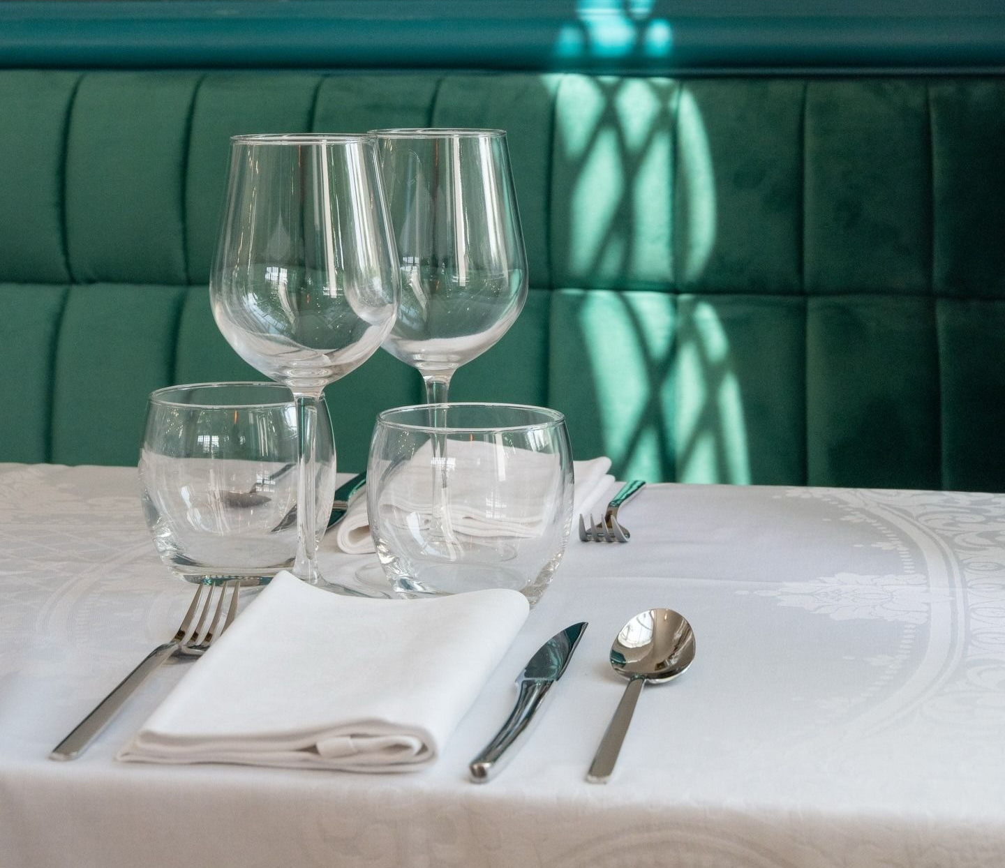Élégante table de restaurant dressée avec verres à vin, verres à eau, couverts et serviette blanche sur une nappe blanche.