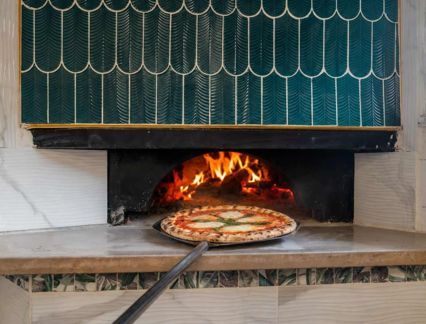 Cuisson de pizzas dans un four à bois avec des flammes et une pelle à pizza en métal devant.