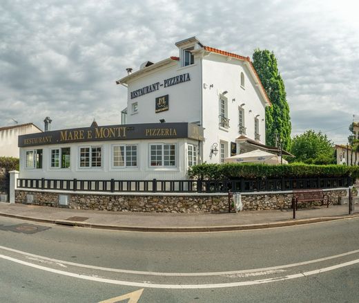 Bâtiment blanc d'un restaurant en bord de route, avec une enseigne noire et un mur de pierre, sous un ciel nuageux.