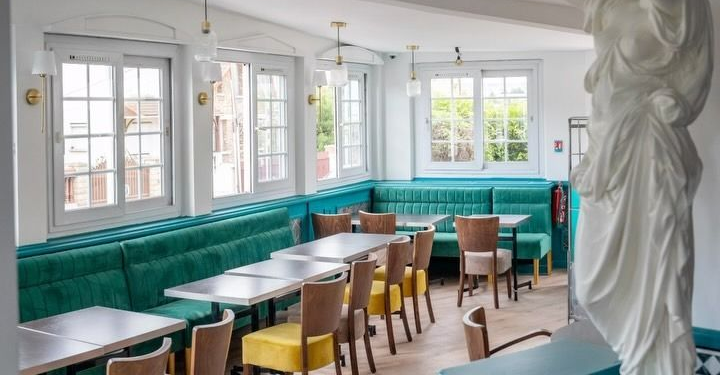 Intérieur lumineux de café avec banquettes turquoise, tables et chaises blanches et grandes fenêtres.