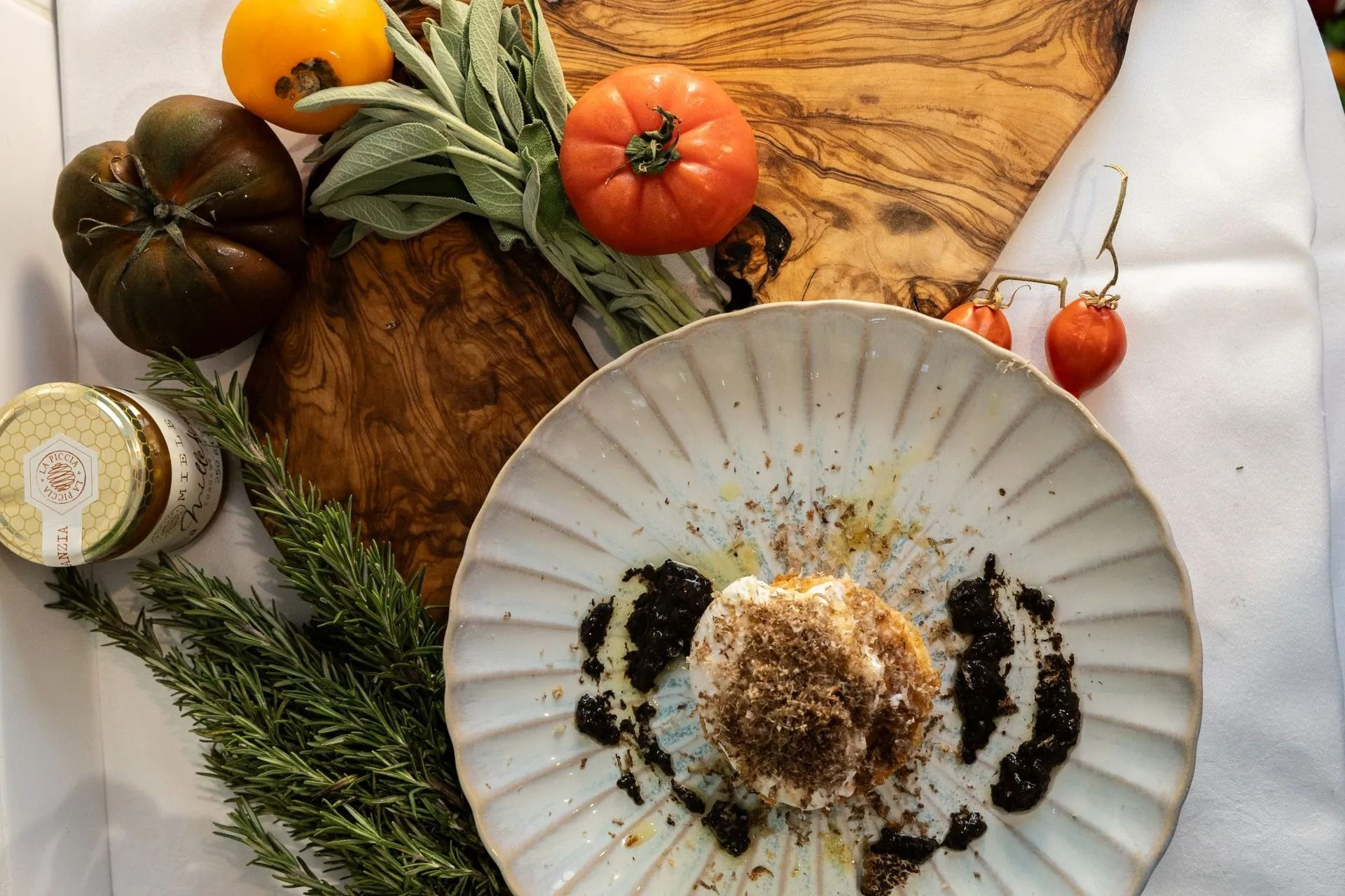 Composition rustique avec des citrouilles, des herbes aromatiques, un bocal et un dessert présenté sur une nappe blanche.