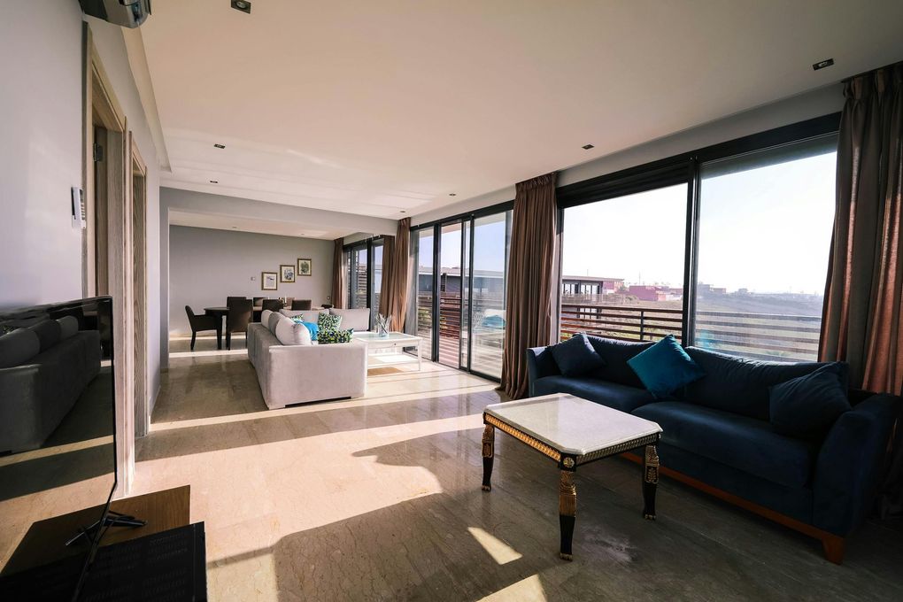 Wohnzimmer mit blauem Sofa, Couchtisch und großen Fenstern mit Blick auf die Stadt.