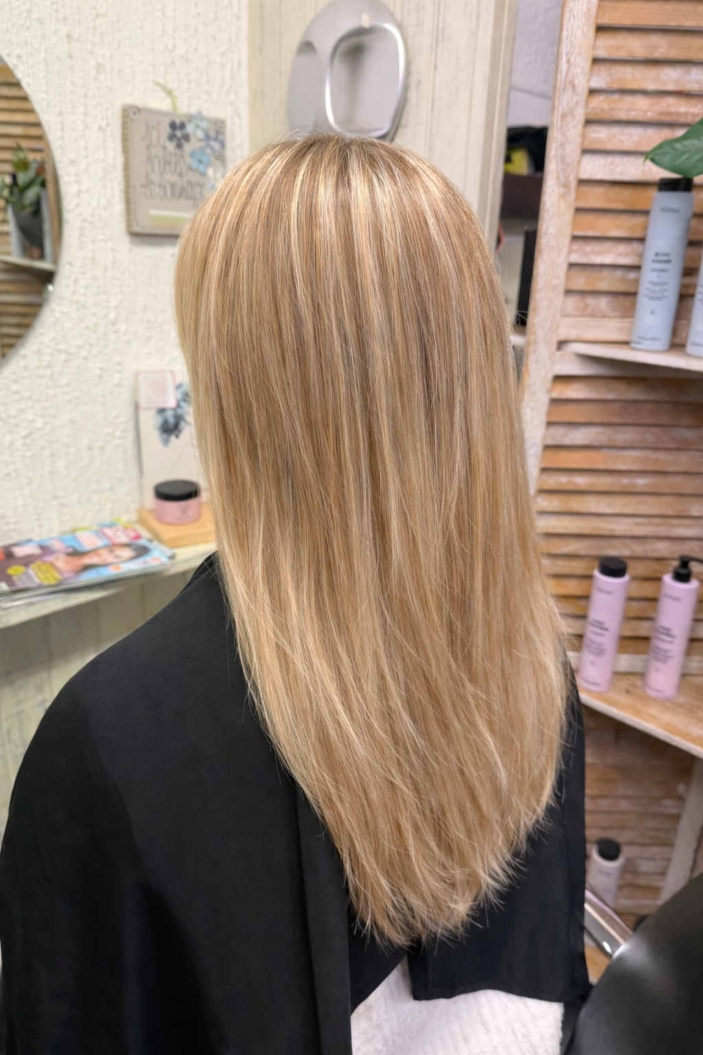 Vue de dos d'une personne aux cheveux raides, blonds méchés, assise sur un fauteuil de salon de coiffure.