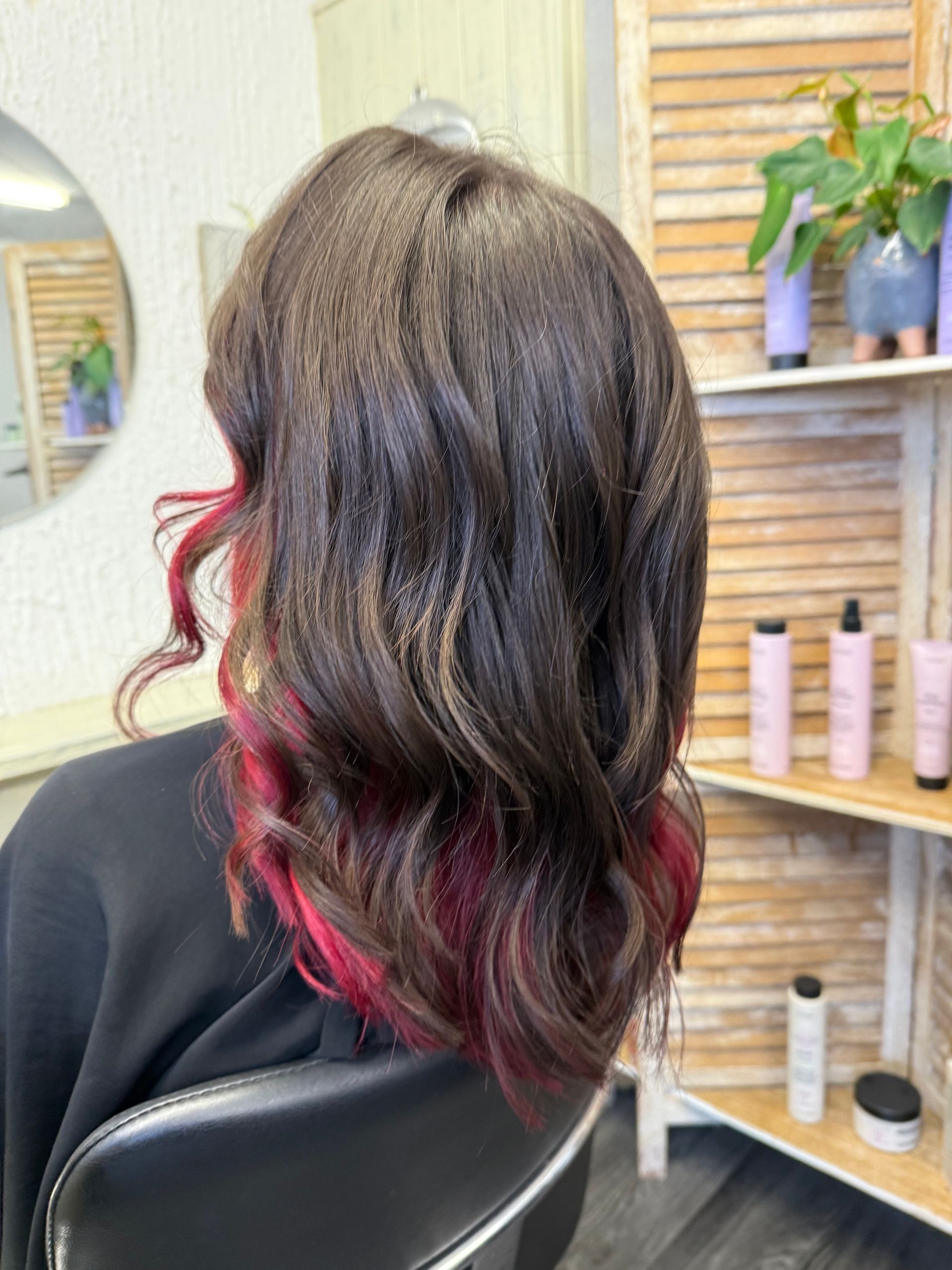 Cheveux ondulés foncés avec des reflets magenta, assis sur un fauteuil de salon, vus de dos