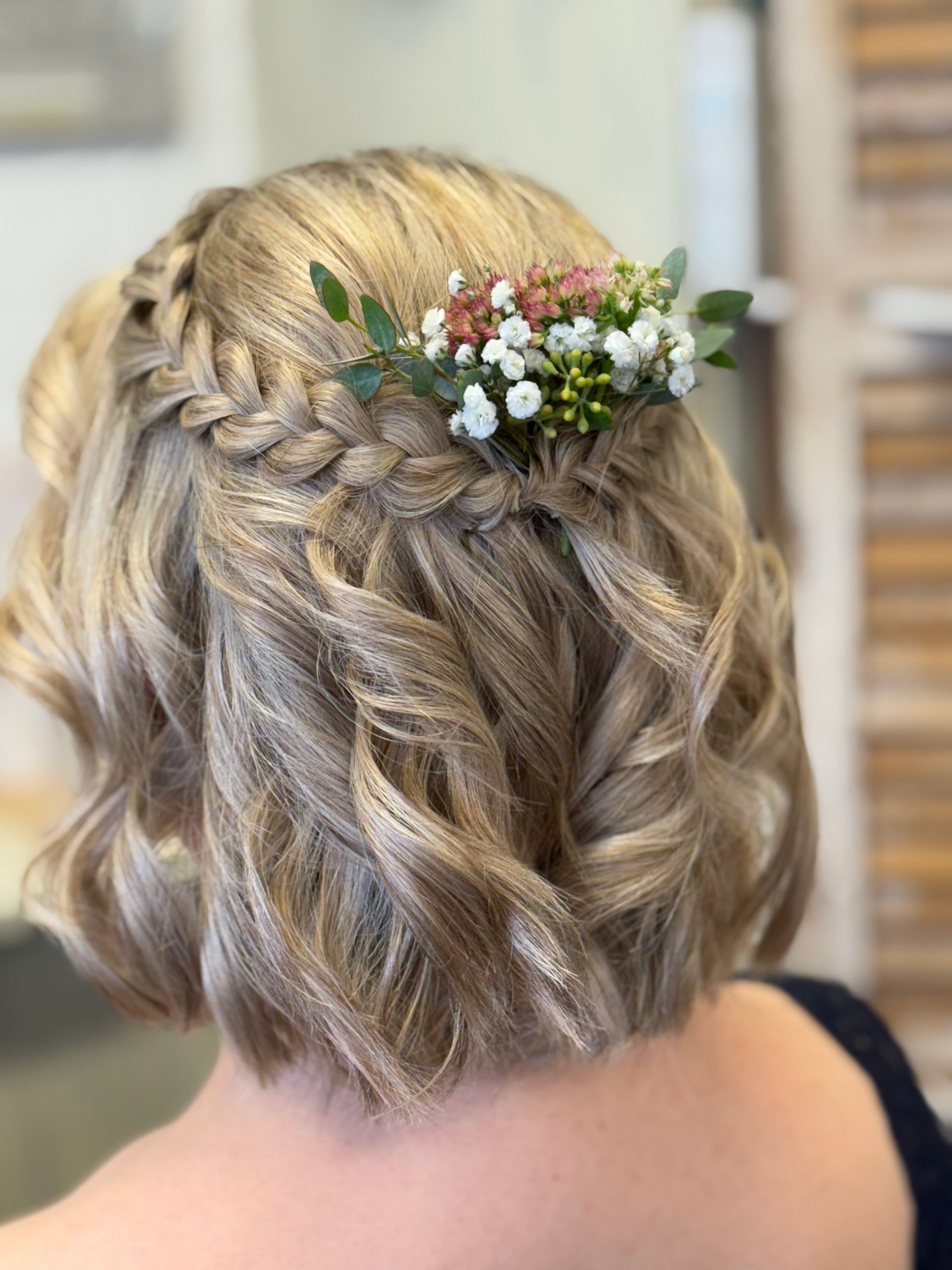 Coiffure blonde tressée mi-attachée avec de petites fleurs blanches et roses à l'arrière