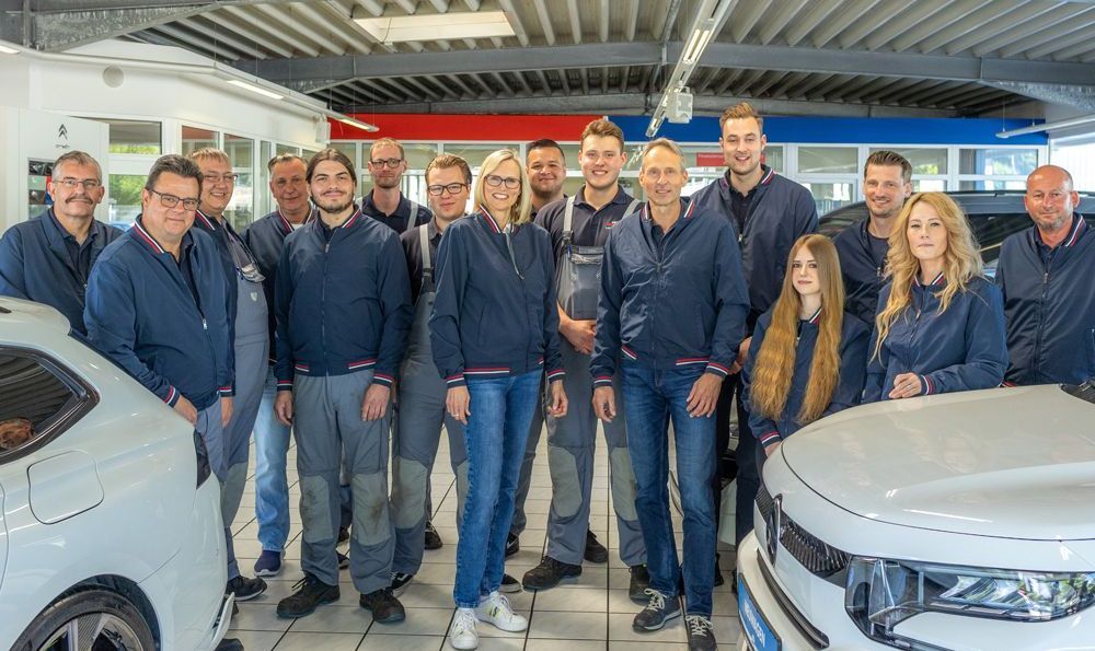 Eine Gruppe von Menschen posiert für ein Foto vor einem weißen Auto.