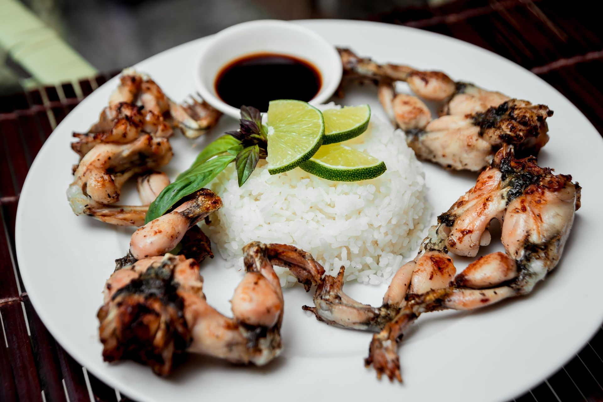 Un plato de ancas de rana a la parrilla servido con una porción de arroz blanco, rodajas de lima