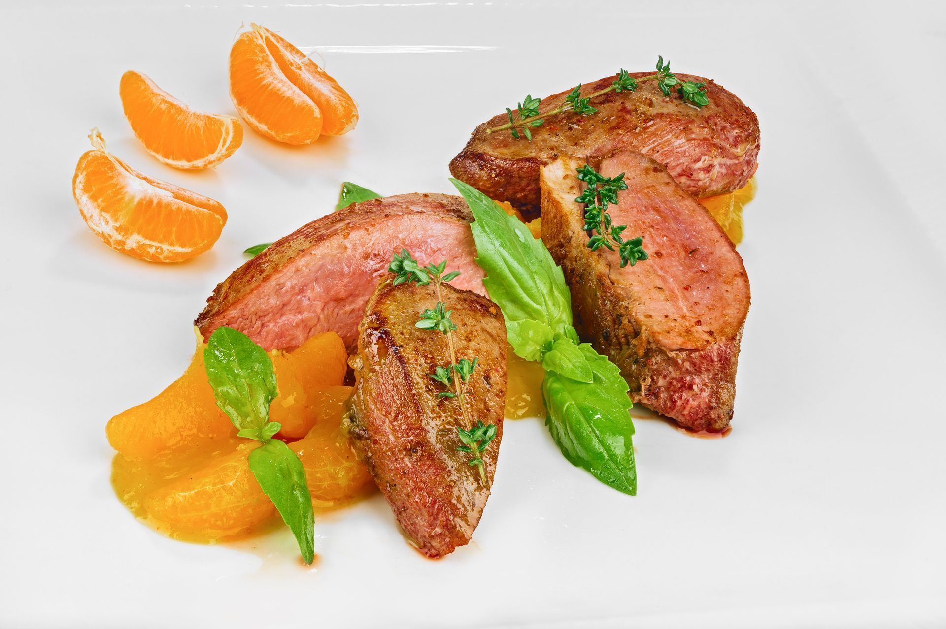 Tres lonchas de pechuga de pato sellada a la sartén, aderezadas con hierbas aromáticas y servidas con gajos de naranja 