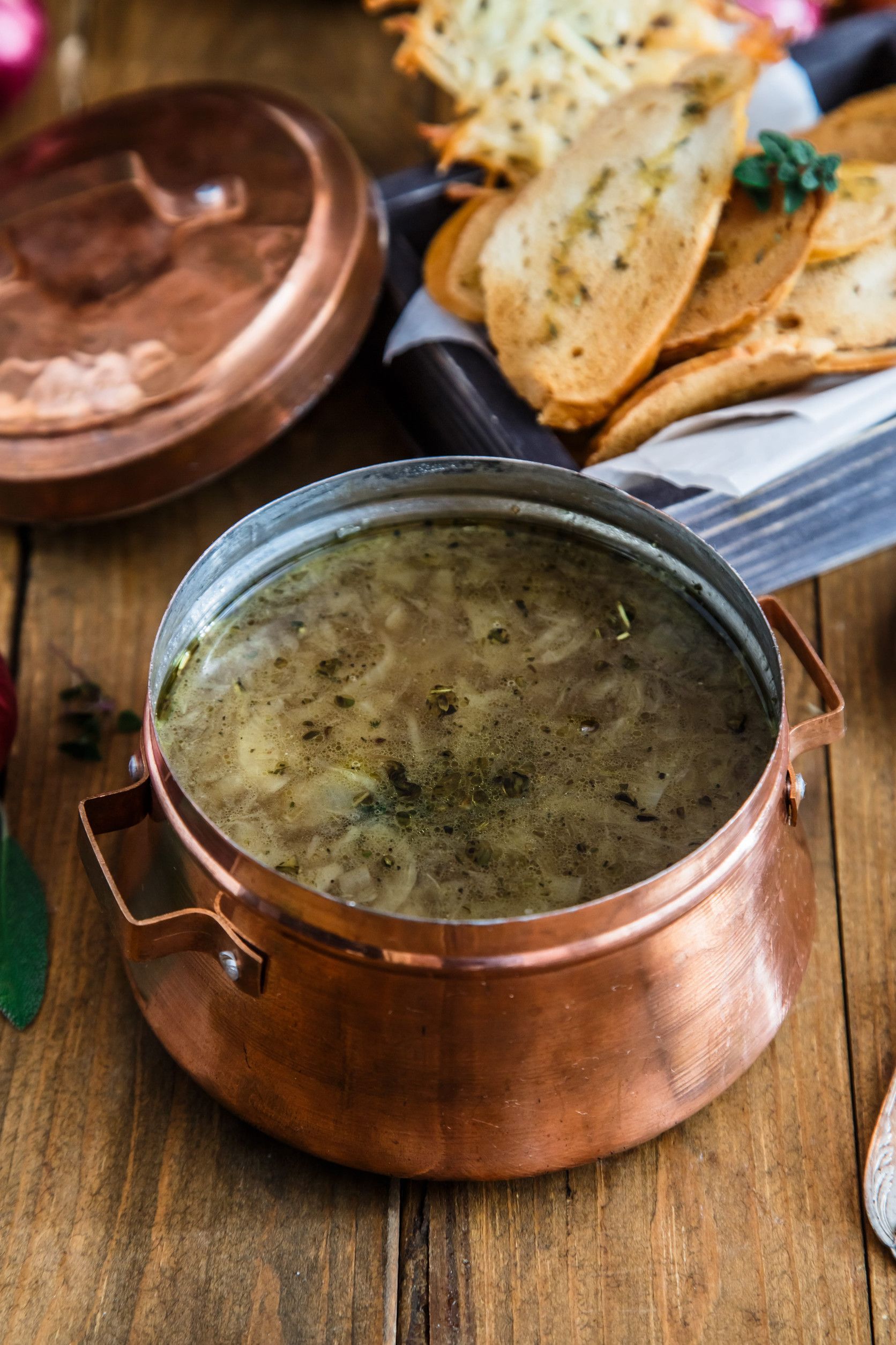 Un tazón de sabrosa sopa de cebolla en una olla de cobre, acompañada de rebanadas de baguette tostadas
