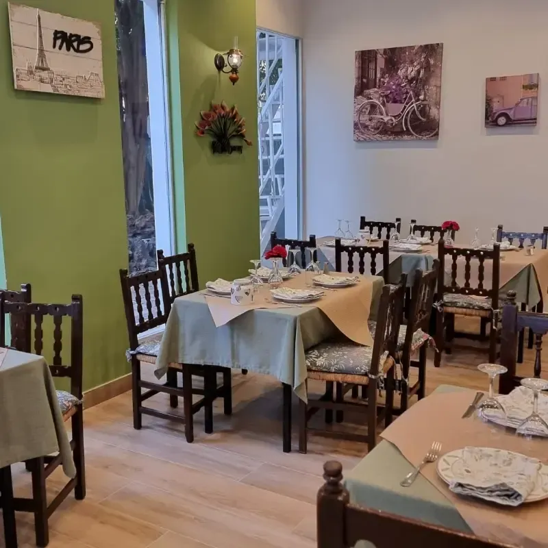 El interior de un restaurante con mesas de madera puestas con platos, paredes de color verde claro y decoración