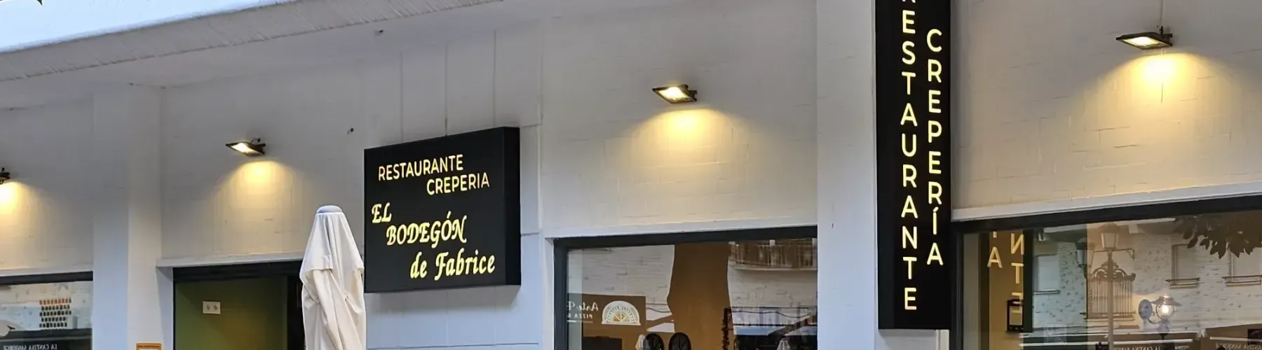 Vista exterior de un restaurante con letrero negro con texto amarillo que dice 