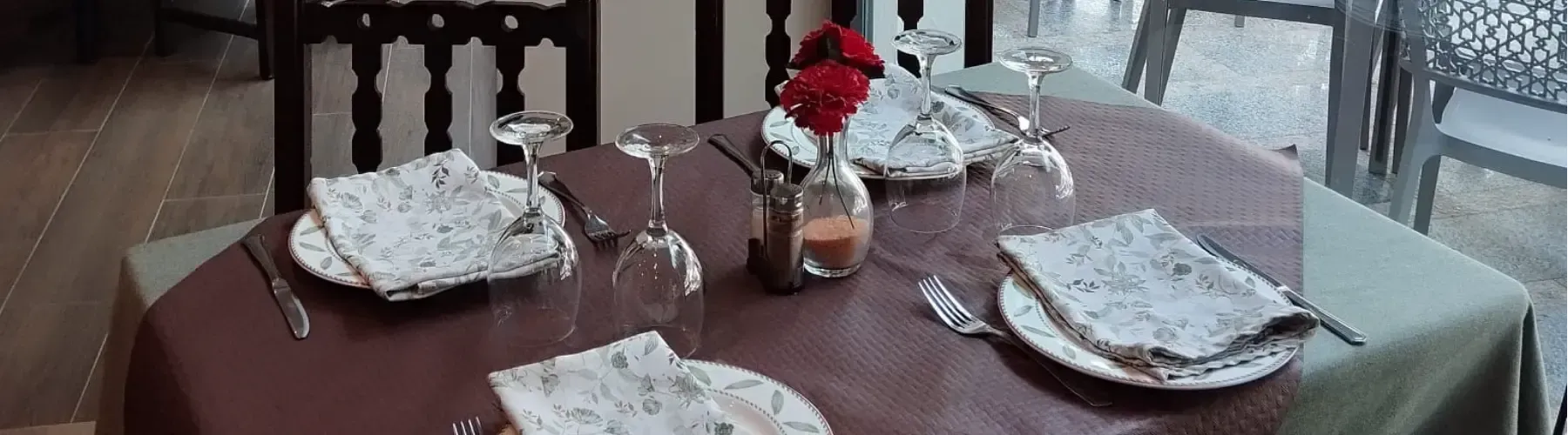 Una mesa de comedor puesta para tres personas con servilletas blancas estampadas, copas de vino
