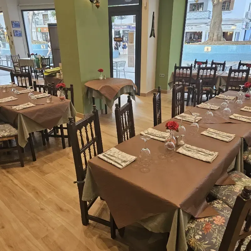 Un comedor interior de restaurante con varias mesas con manteles marrones, sillas de madera y cojines florales.