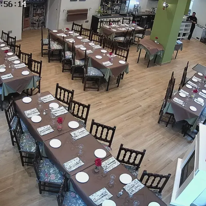 Comedor vacío con varias mesas rectangulares largas cubiertas con manteles marrones y puestas con platos