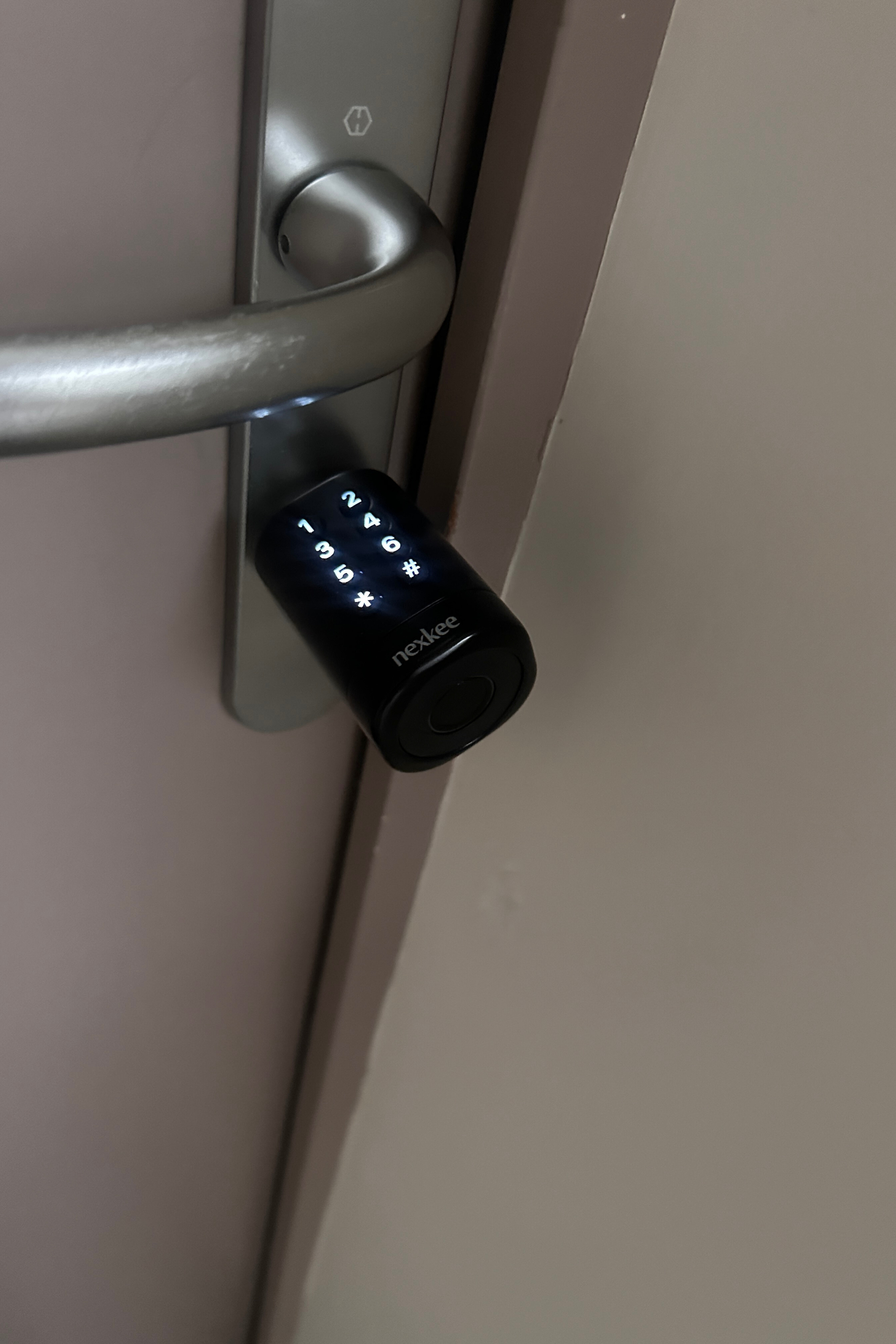 Serrure à clavier noire sur poignée de porte avec poignée argentée. Chiffres lumineux visibles.