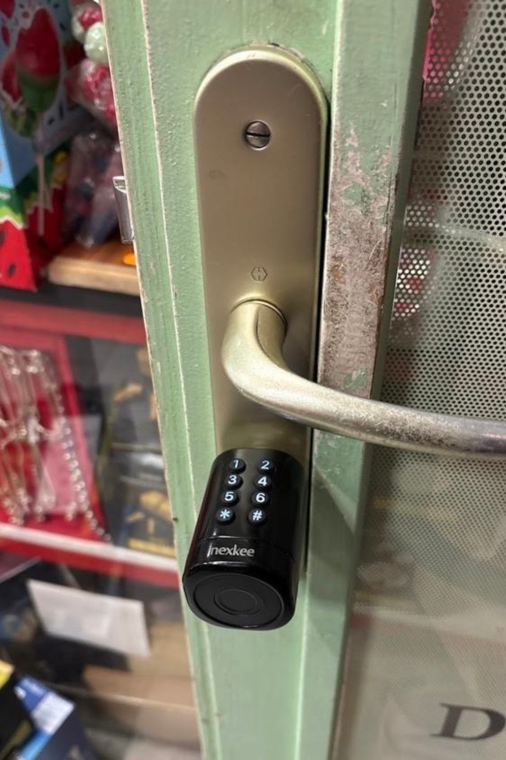 Poignée de porte avec serrure à clavier. La poignée est montée sur une porte verte. Le clavier est noir.