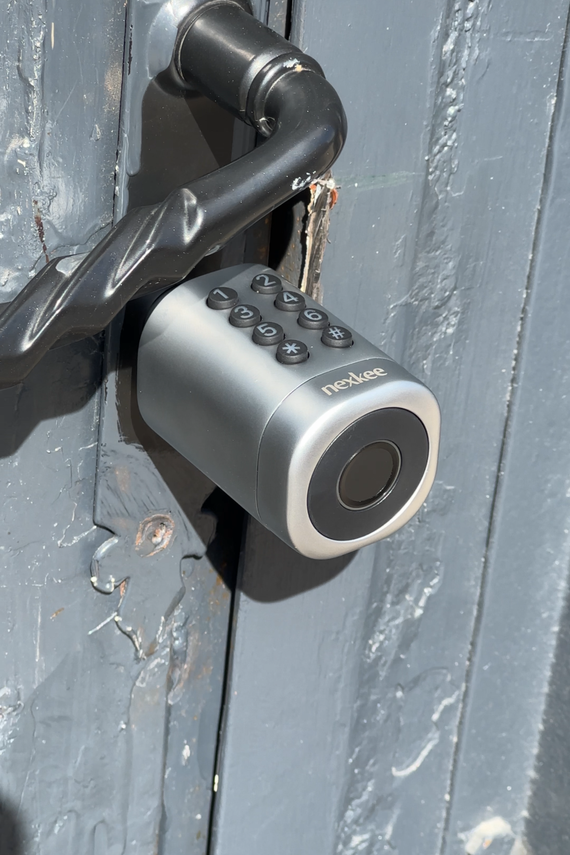 Serrure de porte numérique argentée avec lecteur d'empreintes digitales sur une porte grise.