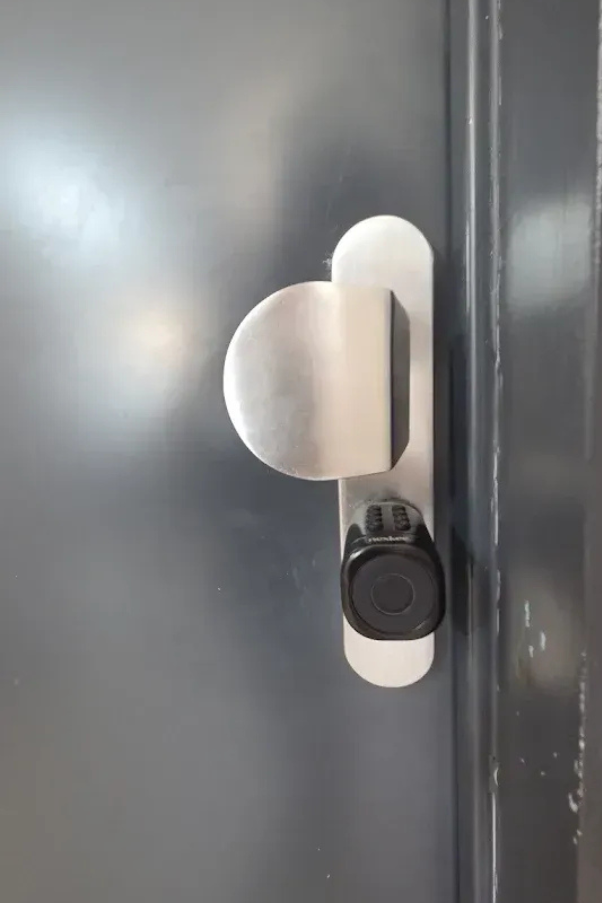 Poignée de porte argentée avec un porte-clés noir attaché à une porte grise.