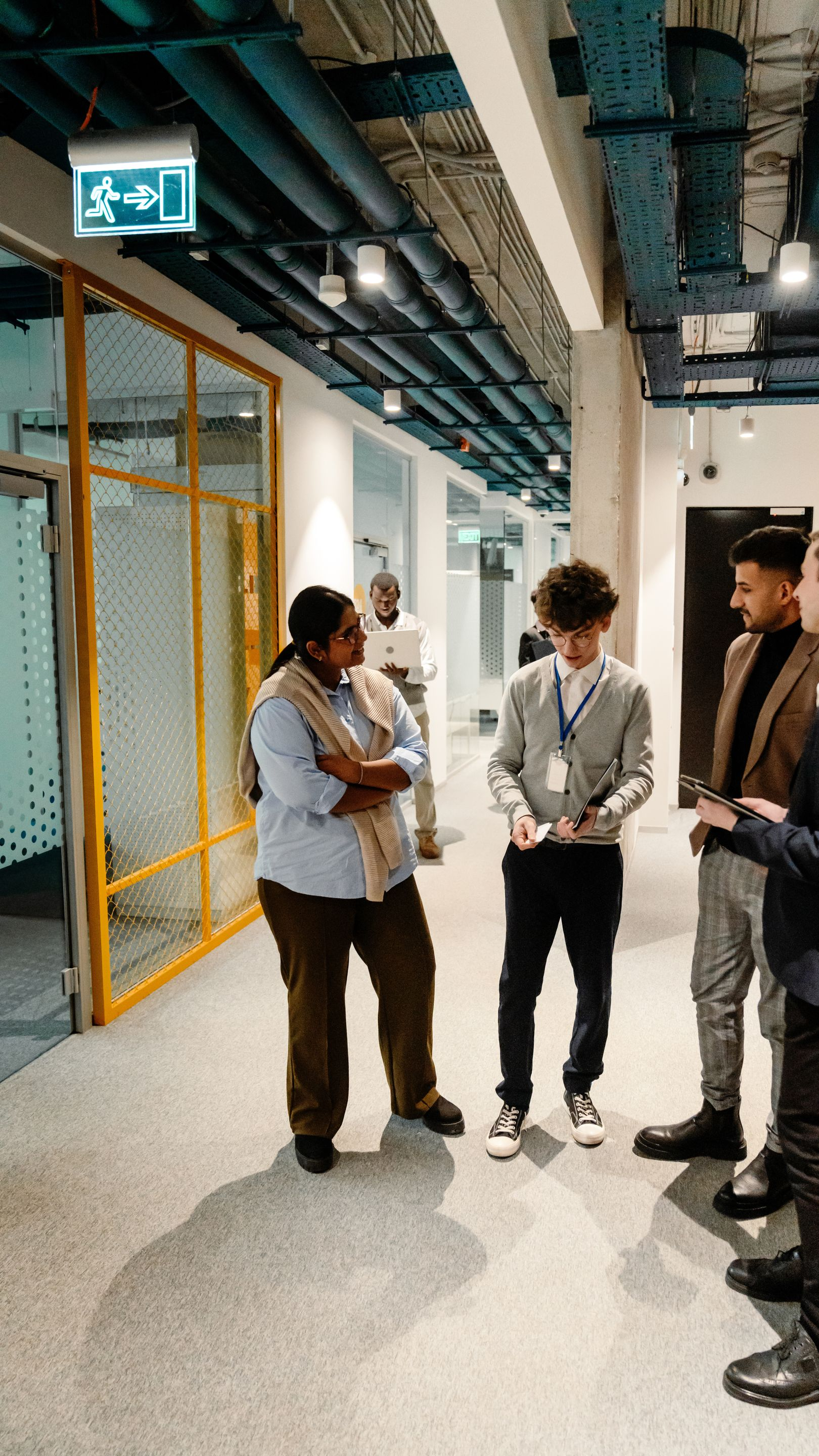 Des gens discutent dans un couloir de bureau bien éclairé. Une femme, les bras croisés, d'autres tiennent des papiers.