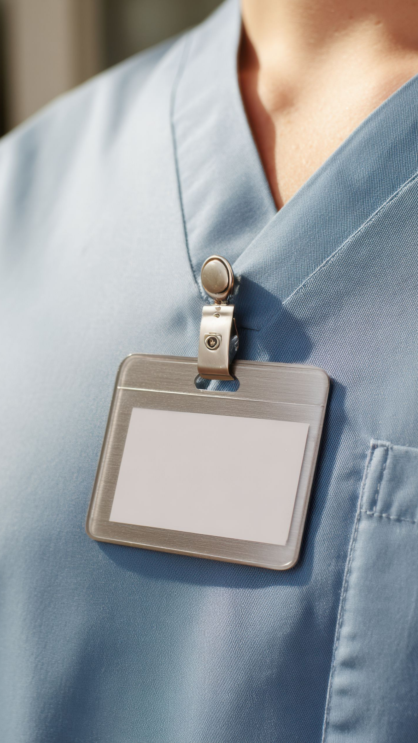 Étiquette nominative argentée accrochée à l'uniforme bleu clair d'un professionnel de la santé.