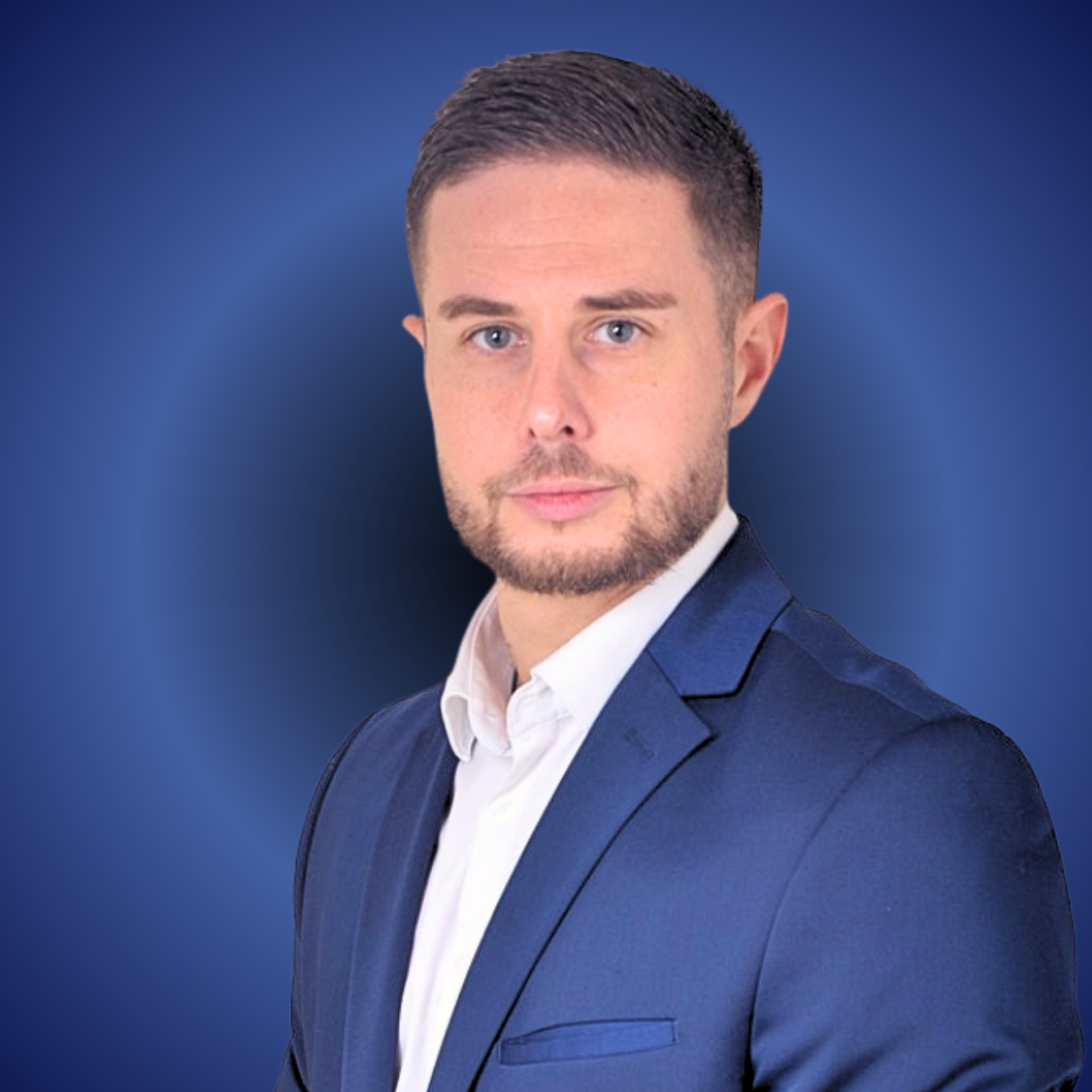 Un homme en chemise bleue assis sur une chaise noire, regardant la caméra.