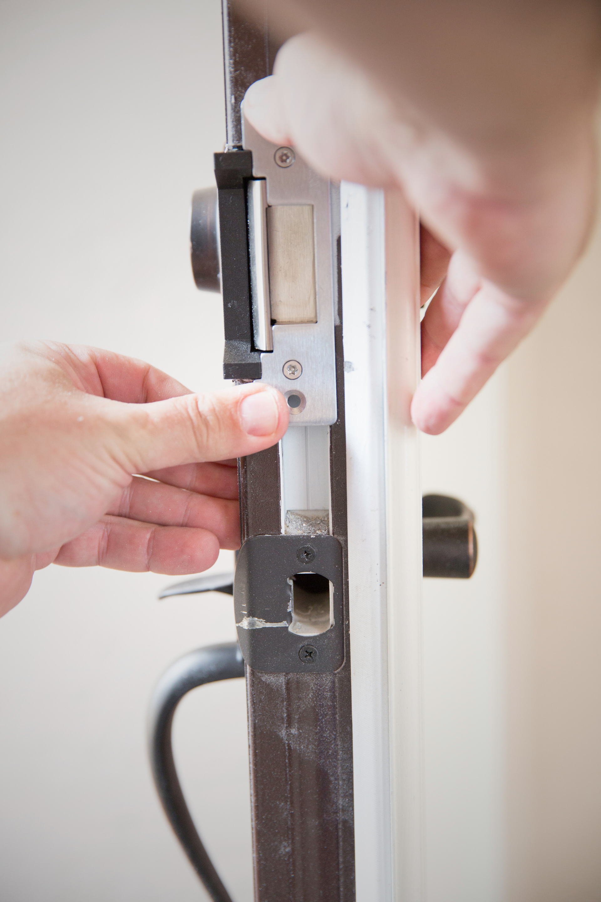 Mains installant un loquet de porte sur un cadre de porte marron foncé.