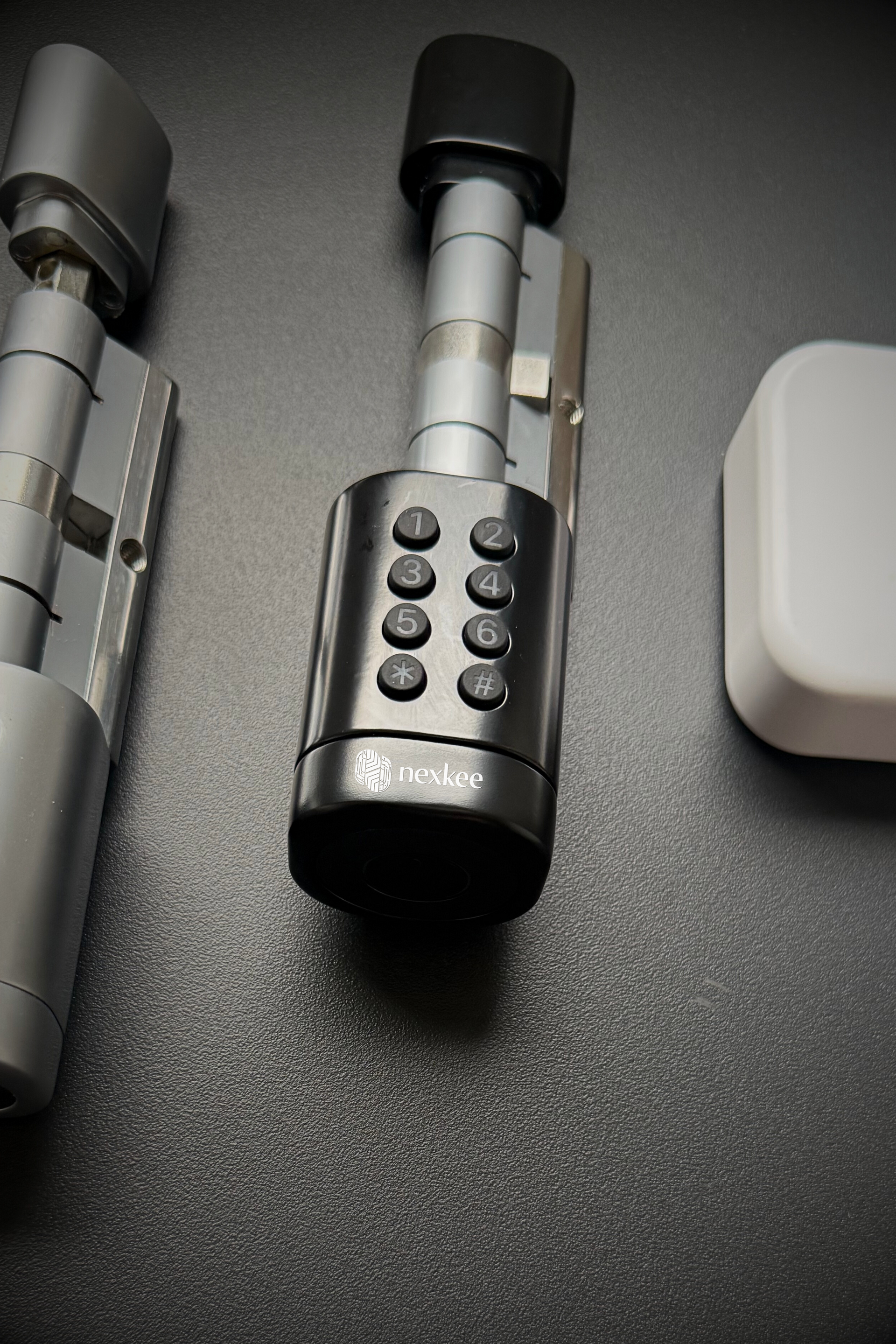 Serrure de porte numérique avec clavier et dispositif carré blanc, sur une surface sombre.