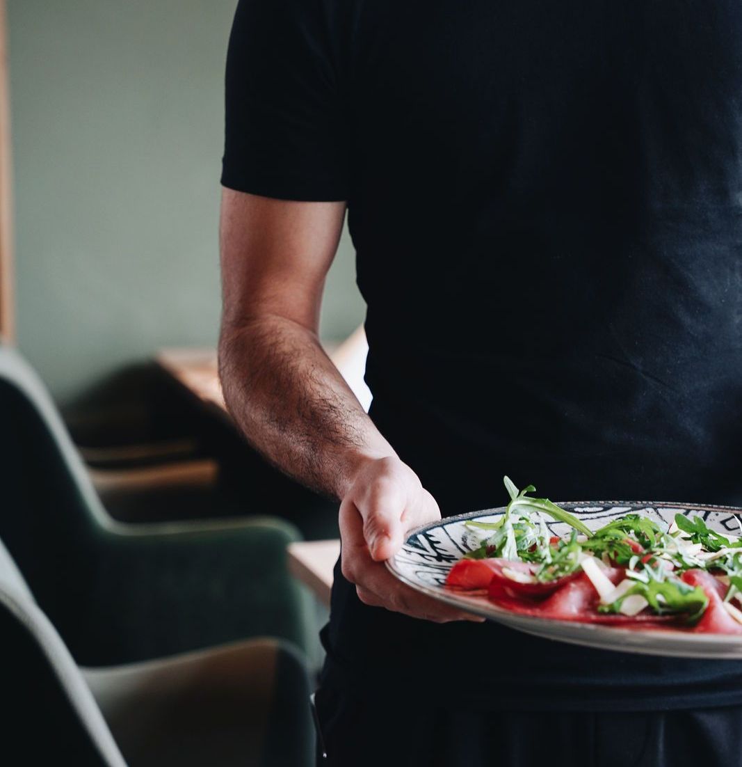 Kellner hält einen Teller mit Carpaccio und Rucola.