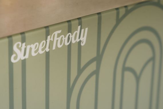 Salbeigrüner Hintergrund mit vertikalen Streifen, geschwungenen Linien und dem weißen Schriftzug „StreetFoody“ oben links.