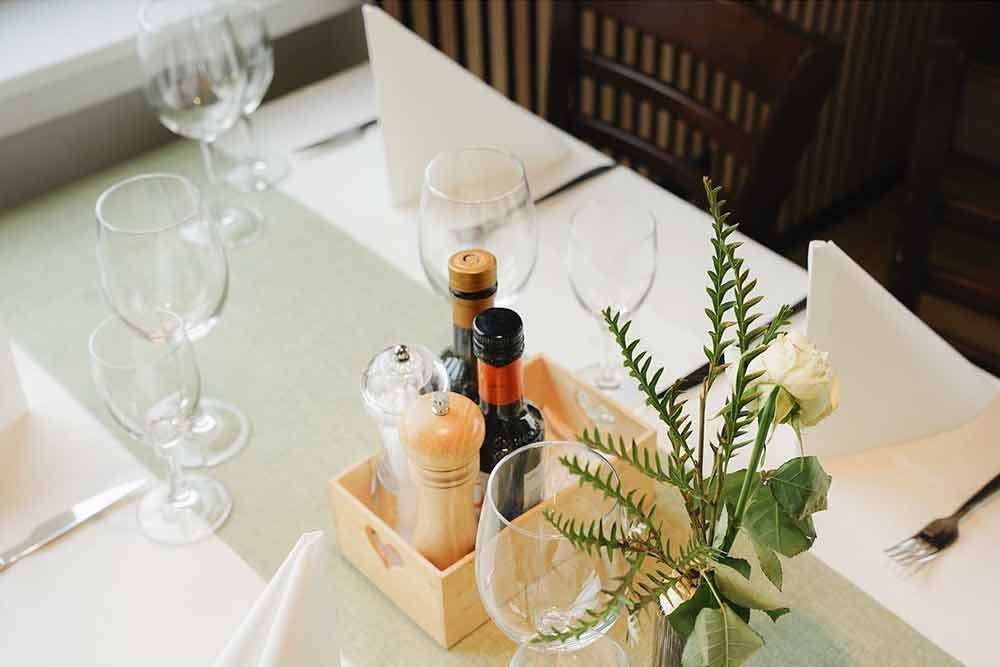 ein Tisch mit einer Flasche Wein, Gläsern, Salz- und Pfefferstreuern und einer Vase mit Blumen.